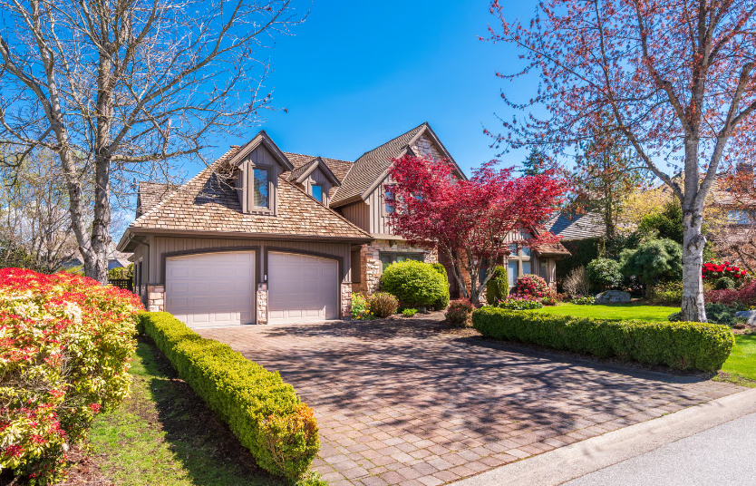 A luxury Tudor-style house with a brick driveway, two-car garage, and vibrant red Japanese Maple tree in a sunny Chicago neighborhood.