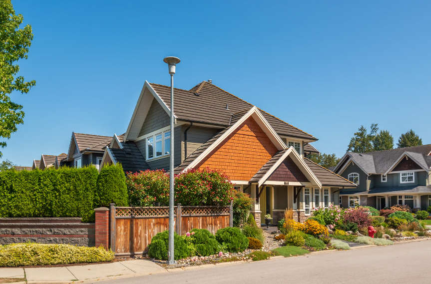 A beautiful modern craftsman-style home with professional landscaping and a wood fence under a clear blue sky.