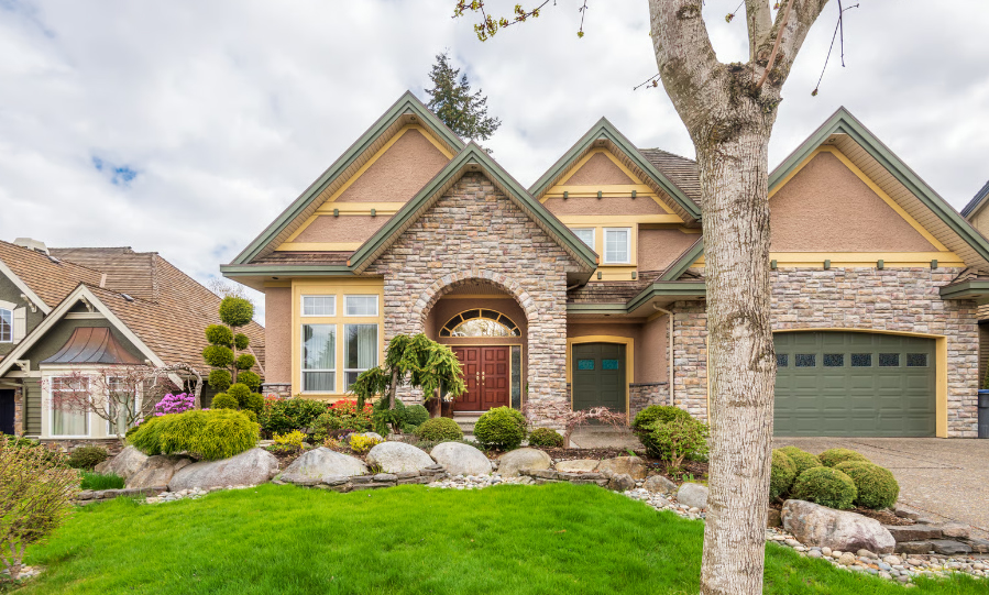 Exterior of a large craftsman home with a multi-gabled roof, stone veneer siding, a grand arched entryway, and a rock garden landscape design.